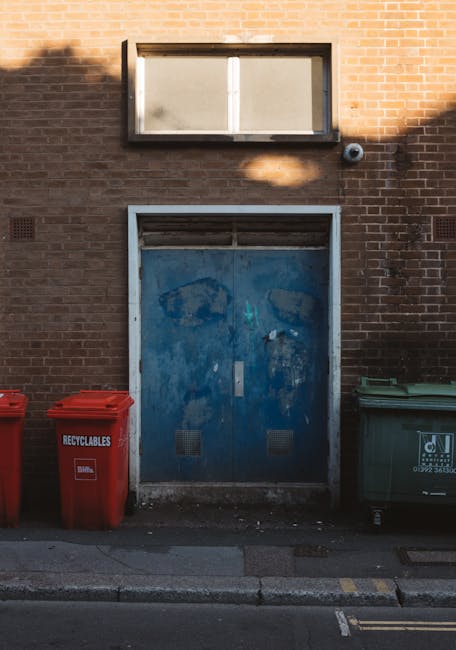 A brick wall featuring a small rectangular window near the top, with a black frame and frosted glass. Below the window, there is a weathered blue metal door with visible patches of paint peeling and r